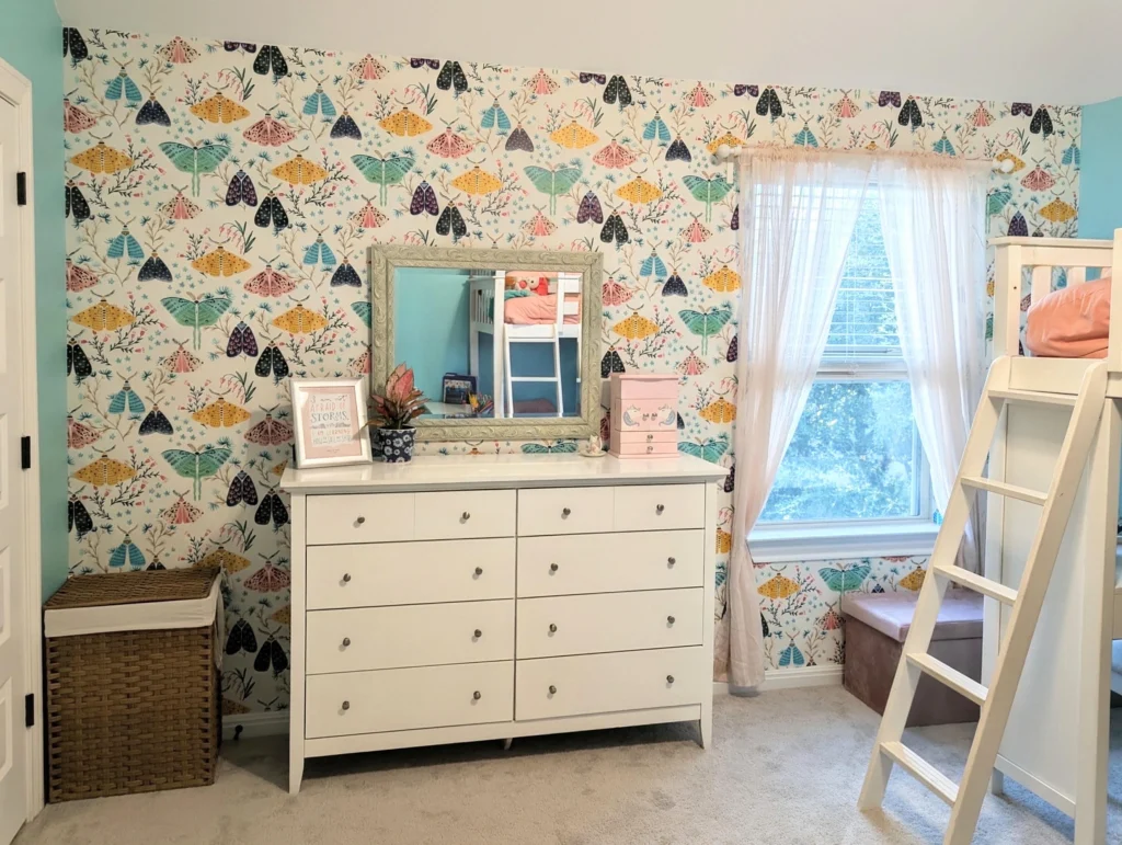A bedroom wall with moth wallpaper and frog pond color paint, with a dresser and a window.
